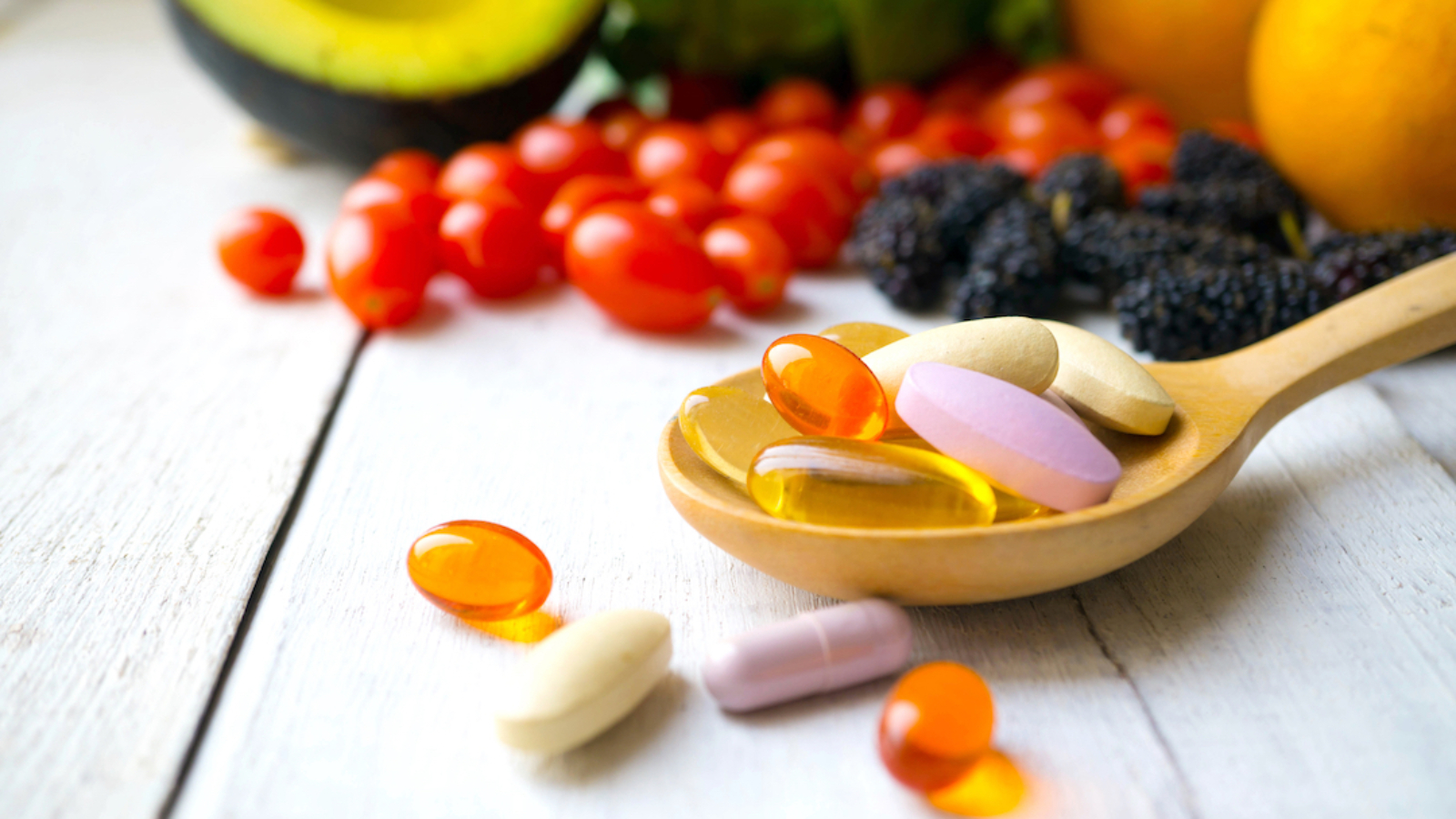 Pills and capsules in wooden spoon with fresh fruits.Multivitamins and supplement from fruits concept.