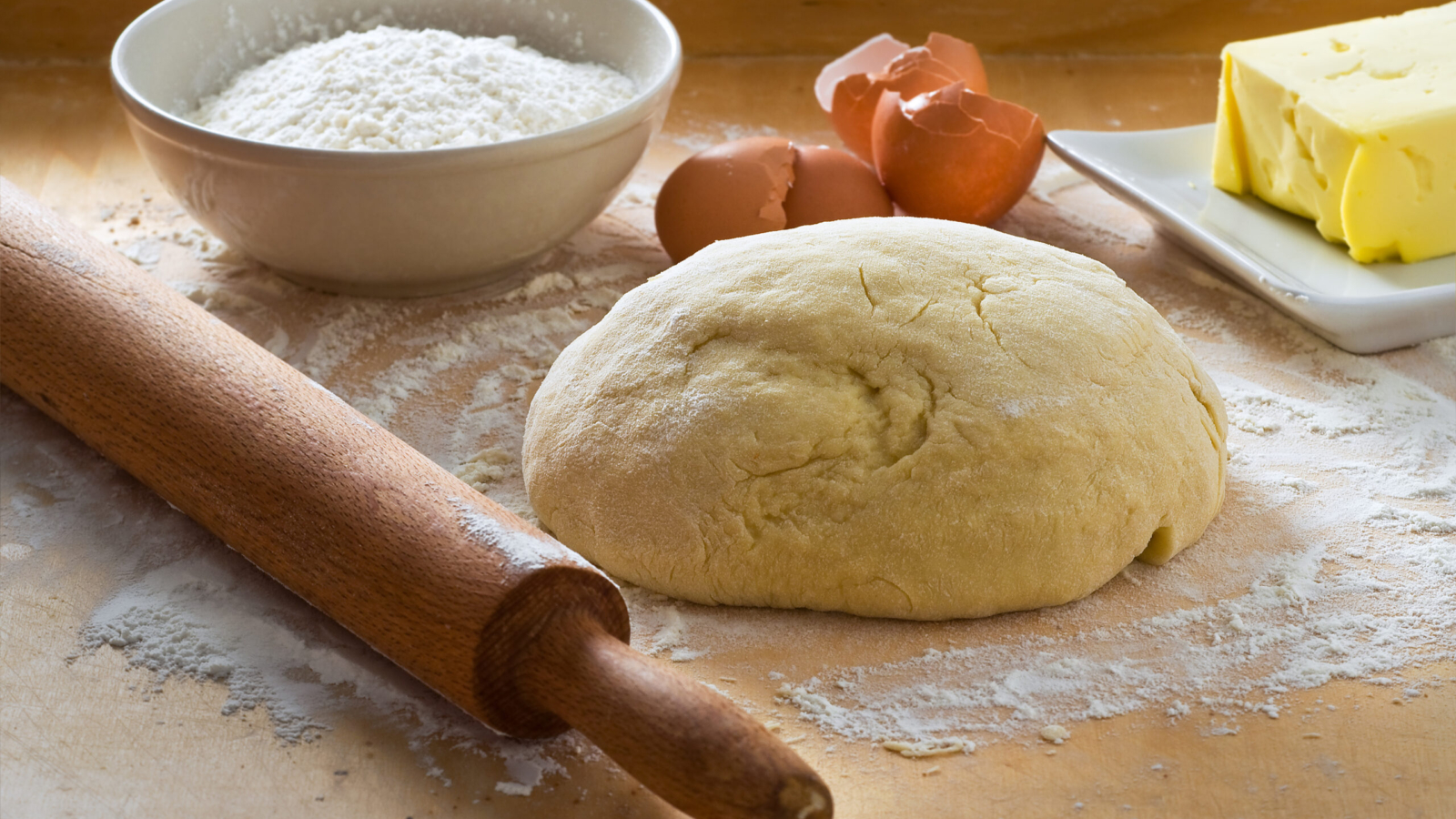 Dough on wooden board with rolling pin.