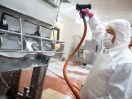 Man washing machines at a factory with a hose