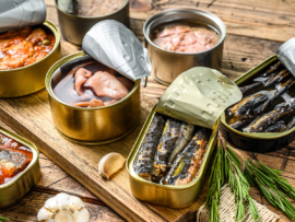 Various canned  fish and seafood in a metal cans. Wooden background. Top view.