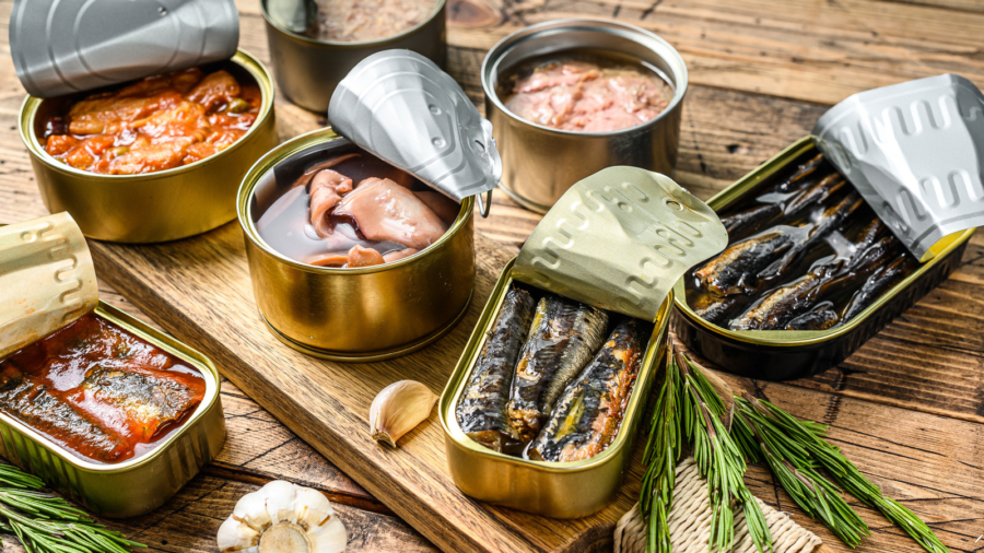 Various canned  fish and seafood in a metal cans. Wooden background. Top view.